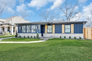 A modern two-story house with a stone foundation, large windows, and a well-maintained lawn.