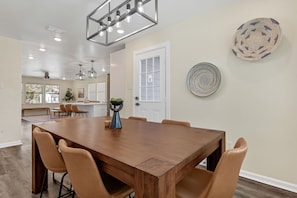 A dining area with a large wooden table, six chairs, pendant lighting, and decorative plates on the wall.