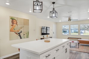 A modern kitchen with a large island, pendant lights, a flat-screen TV, and a dining area with a bench.