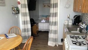 Kompakti keittiö, jossa on kaasuliesi, pesuallas sekä ruokailutila, jossa on pöytä ja tuolit.
