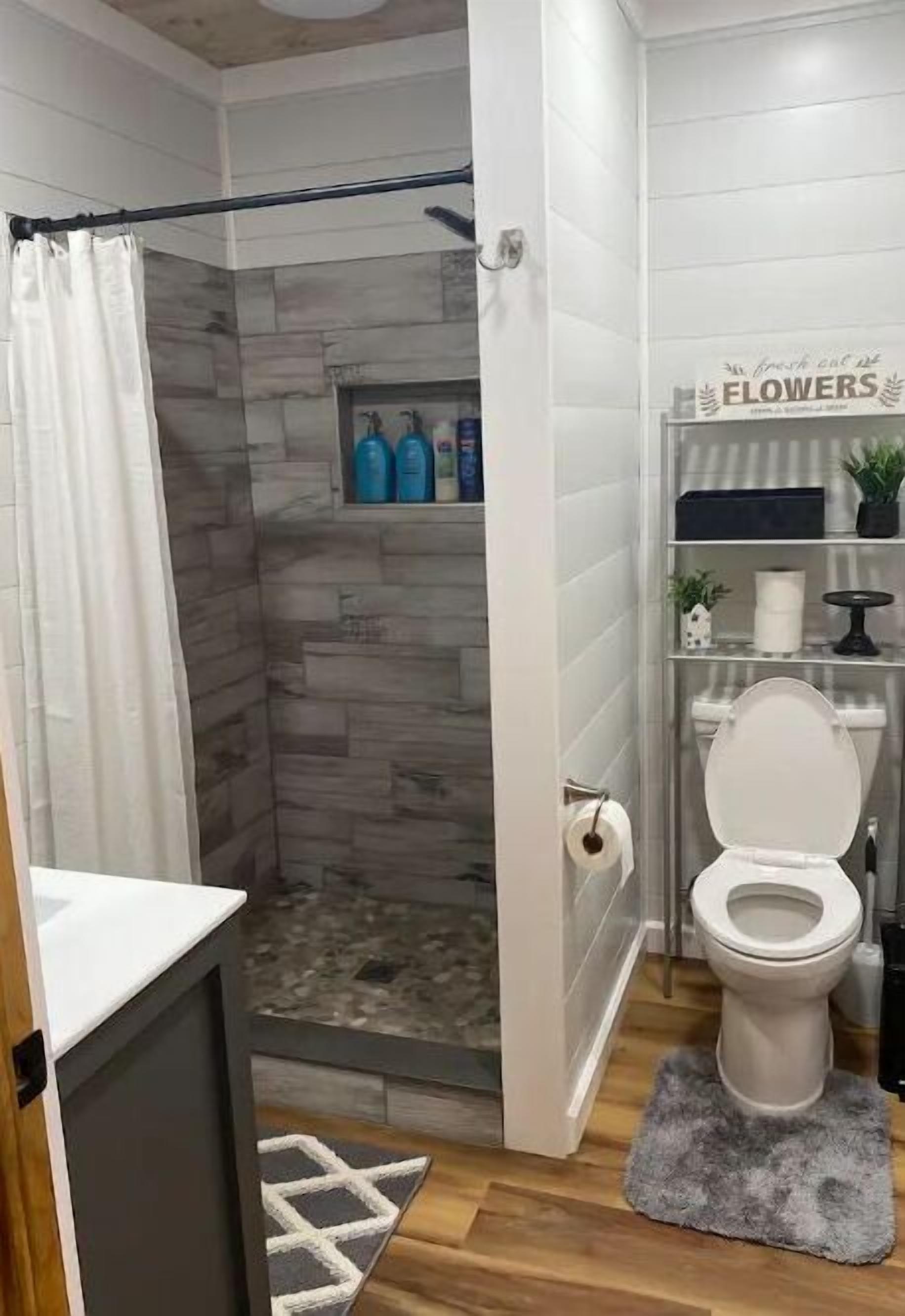 Une salle de bain équipée d’une douche, de toilettes et d’une étagère où sont rangés les articles de toilette.