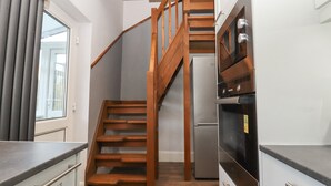 A compact kitchen with a wooden staircase leading to a lofted area. - Albies End (Battle)