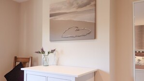 A room with a white desk, a vase with flowers, and a painting of a beach scene. - Albies End (Battle)