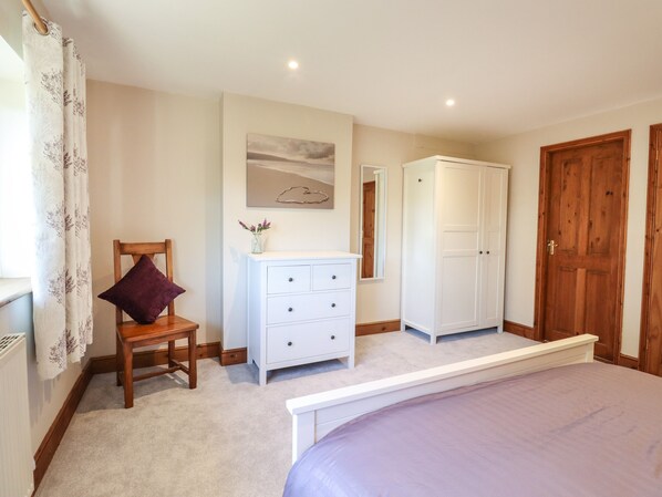 A bedroom with a bed, a wooden chair, a white dresser, a wardrobe, and a window with curtains.