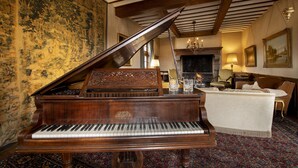 Um piano de cauda em um quarto com carpete estampado, lareira e um sofá.