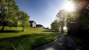 Uma estrada rural leva a um edifício grande e histórico, cercado por vegetação exuberante.