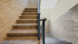 Una escalera con escalones de granito y barandilla de metal negro, que conduce a un rellano con un interruptor de luz.