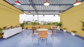 Terraza en la azotea con mesas y sillas, plantas en macetas y vistas a la ciudad.