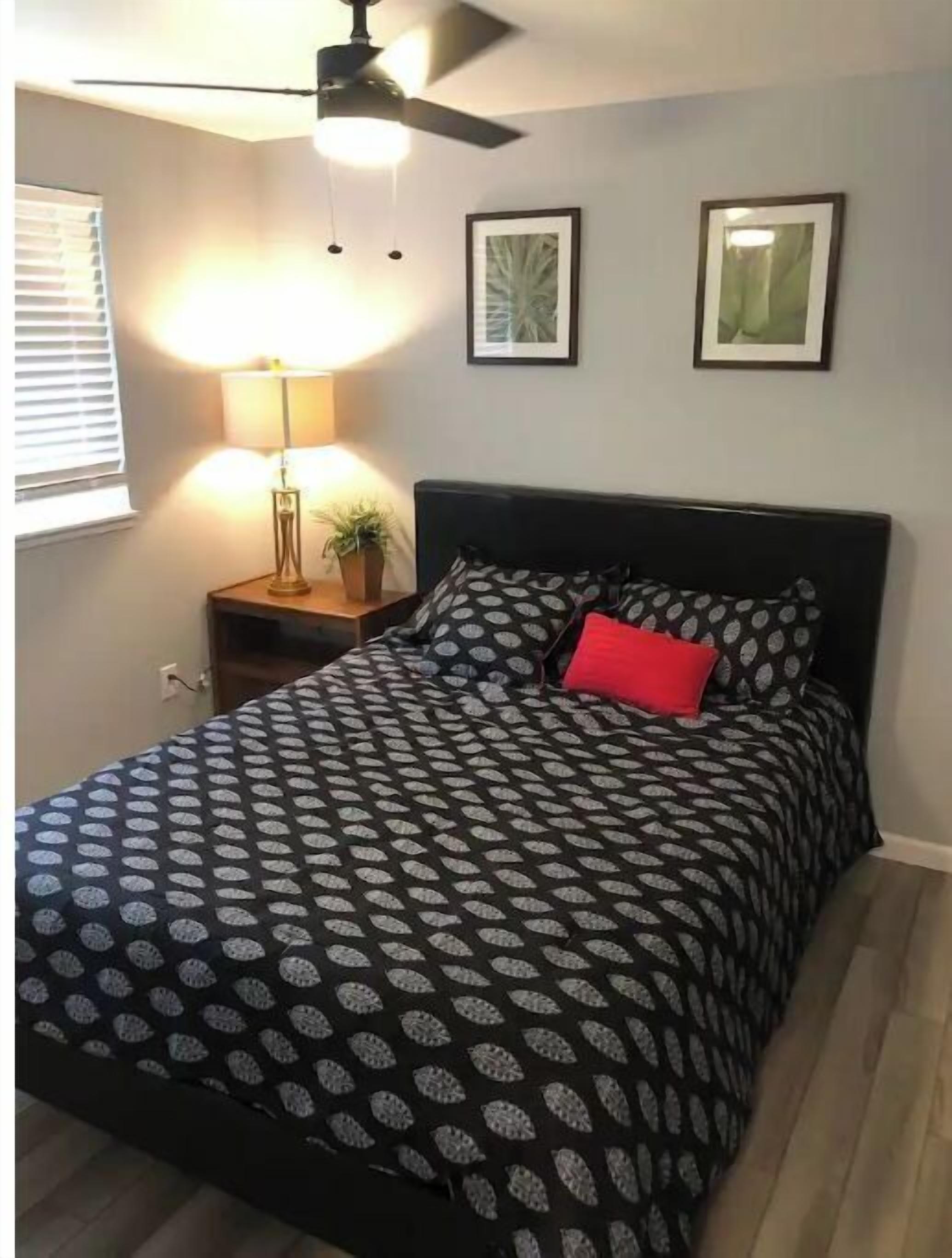 Ein Schlafzimmer mit einem Bett, einem Nachttisch, einer Lampe und zwei gerahmten Bildern an der Wand.
