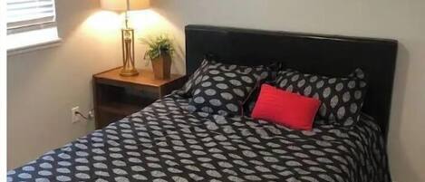 Ein Schlafzimmer mit einem Bett, einem Nachttisch, einer Lampe und zwei gerahmten Bildern an der Wand.