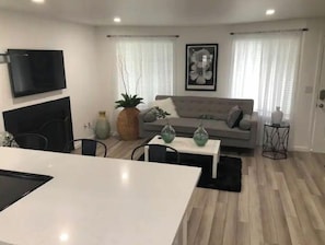 Uma sala de estar moderna com um sofá cinzento, uma mesa de jantar e uma televisão fixada na parede.