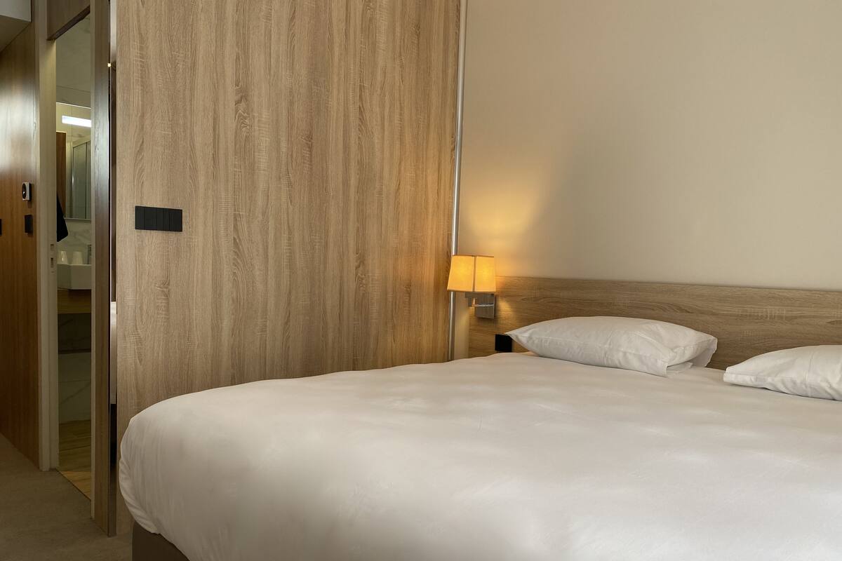 A hotel room with a wooden headboard, a bedside lamp, and a neatly made bed.