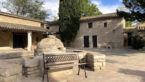 A courtyard with stone benches, a stone fountain, and traditional buildings with tiled roofs and stone walls. - Domaine de la Reynaude (Aurons)
