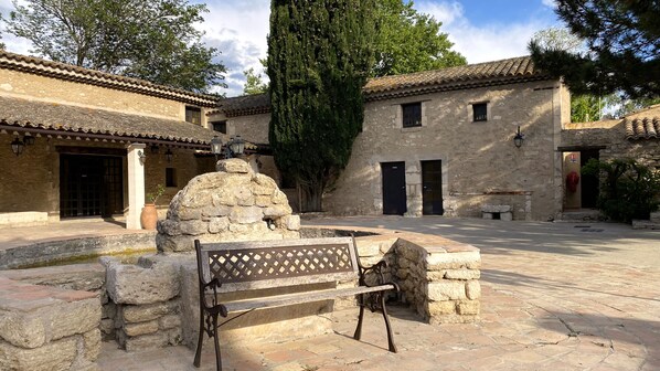 A courtyard with stone benches, a stone fountain, and traditional buildings with tiled roofs and stone walls. - Domaine de la Reynaude (Aurons)