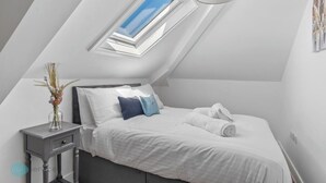 A bedroom with a skylight, a bed with white and blue bedding, a bedside table with a vase, and a hanging light fixture. - The Penthouse By Pureserviced (Plymouth)