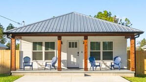 Eine überdachte Veranda mit vier blauen Adirondack-Stühlen, einer weißen Tür und einem Metalldach.