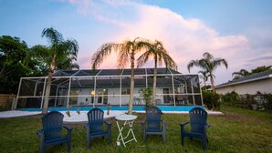 A modern house with a glass-enclosed patio, a swimming pool, and four blue chairs. - Ellie’s Landing 1 – Chill & Grill Dockside Oasis (Port Charlotte)