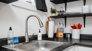 Et moderne køkken med en stålvask, hanefaucet, en plante og køkkenredskaber på bordet.
