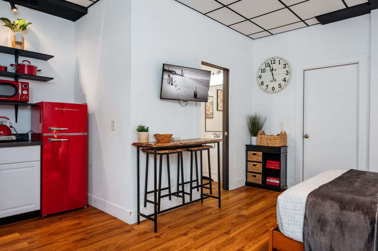 A compact kitchen with a red refrigerator, a microwave, and a wooden bar stool.