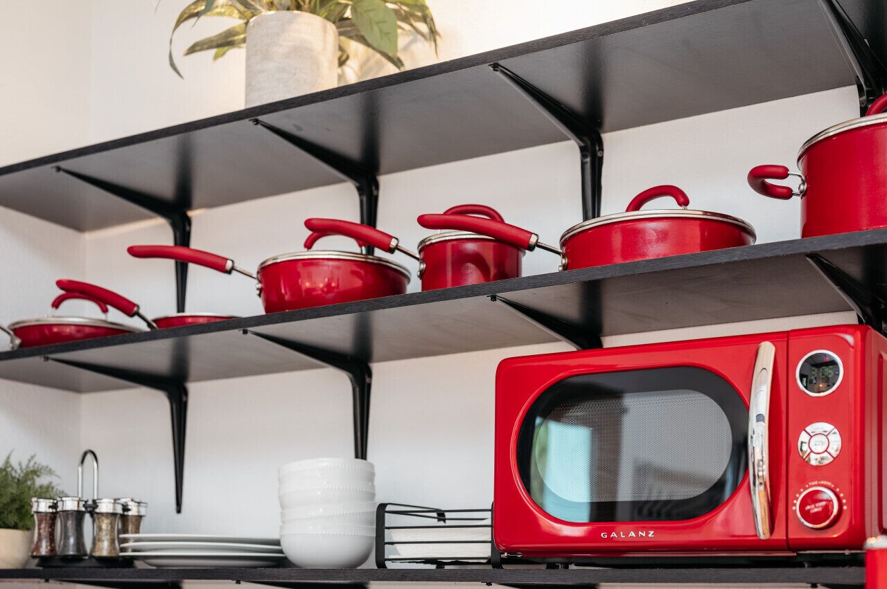 A kitchen with red cookware on shelves, a red microwave, and white dishes on the counter.