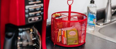 A red coffee maker and a red basket with items on a kitchen counter.