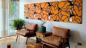 A modern living room with a large abstract painting, wicker furniture, and a view through a window. - 2D Apartment Impeccable - Air Conditioned - Metro Los Héroes (Santiago)