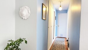 A hallway with a patterned rug, a potted plant, and a framed picture on the wall. - 2D Apartment Impeccable - Air Conditioned - Metro Los Héroes (Santiago)