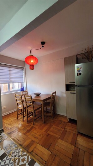 A compact kitchen with a dining table, chairs, a refrigerator, and a red hanging light fixture.