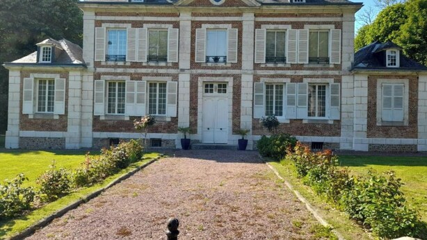 Una casa de dos pisos con fachada simétrica, una entrada central y un camino de grava que lleva a la puerta principal.