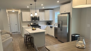 A modern kitchen with white cabinets, stainless steel appliances, and a wooden dining table.