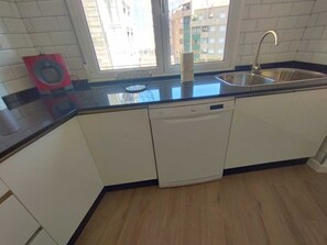 Cozinha com máquina de lavar louça, pia e janela com vista para um edifício.