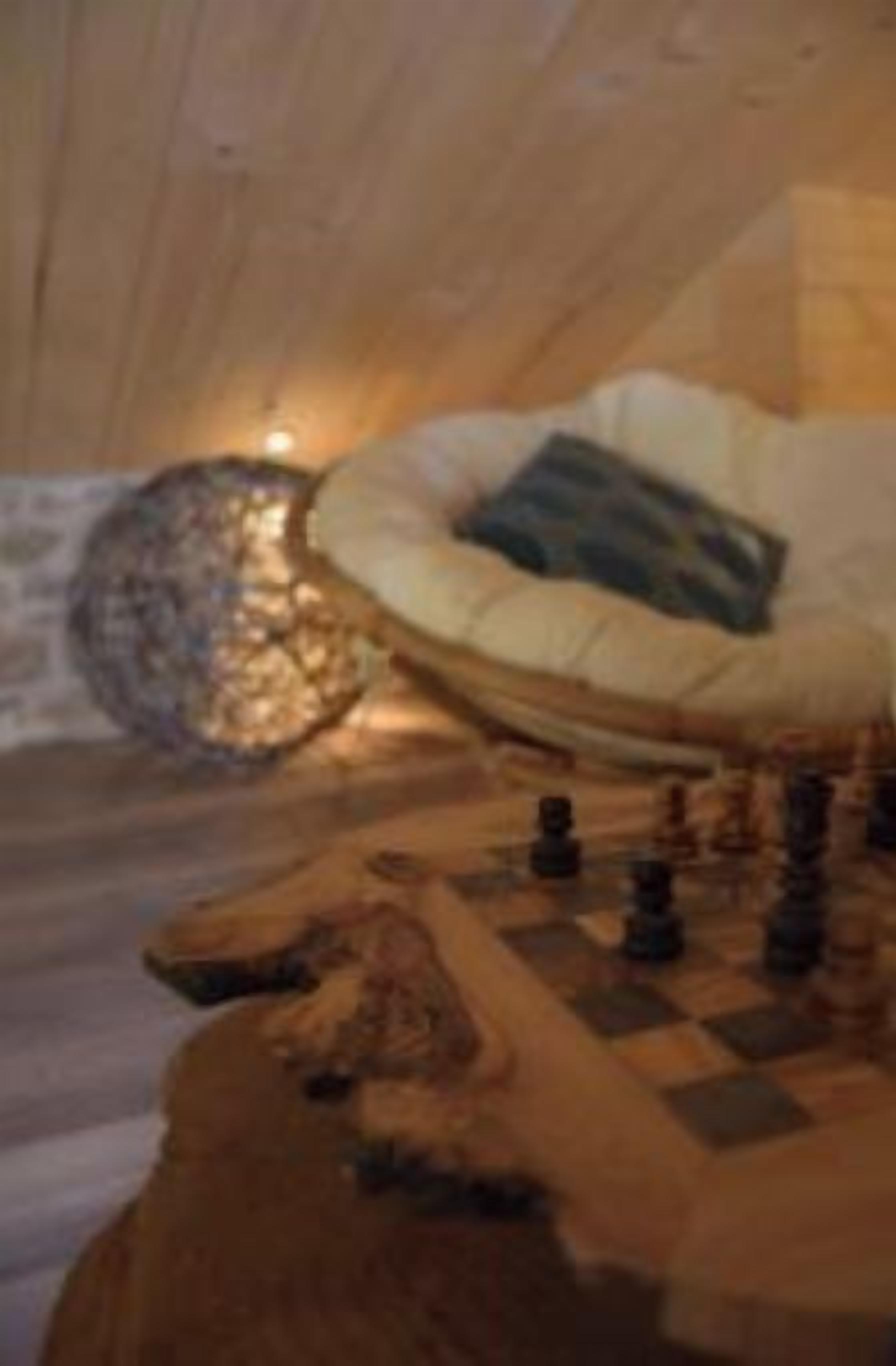 Une pièce chaleureuse avec un lit, une table ronde sur laquelle sont disposés des jeux d’échecs, et un mur en pierre.