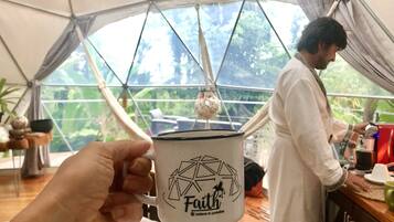 A person holding a mug with a geometric design and the word "Faith" on it. In the background, there is a tent with a view of greenery outside.