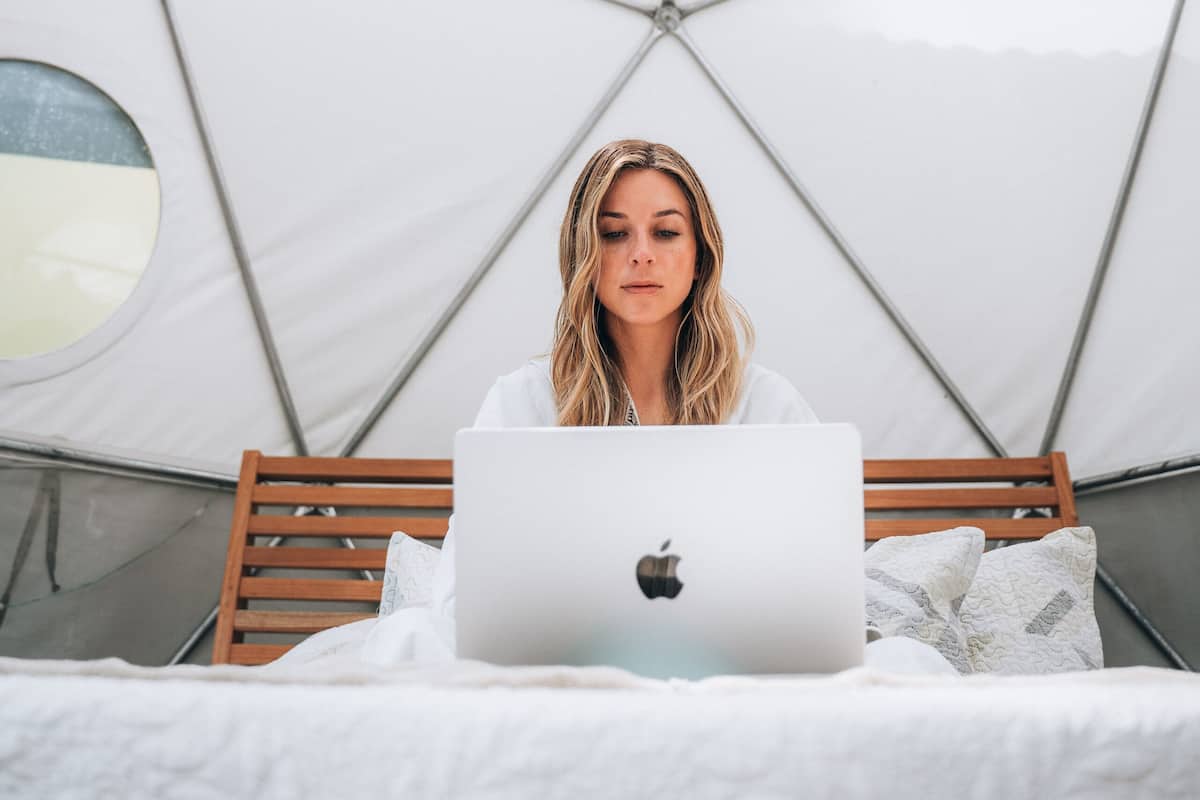 A person sitting on a bed with a laptop, in a room with a geometric ceiling design and circular windows.