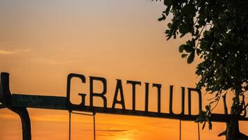 Eine Strandansicht mit einer Schaukel, beschriftet mit 'GRATILUD', und zwei Personen, die darauf sitzen.