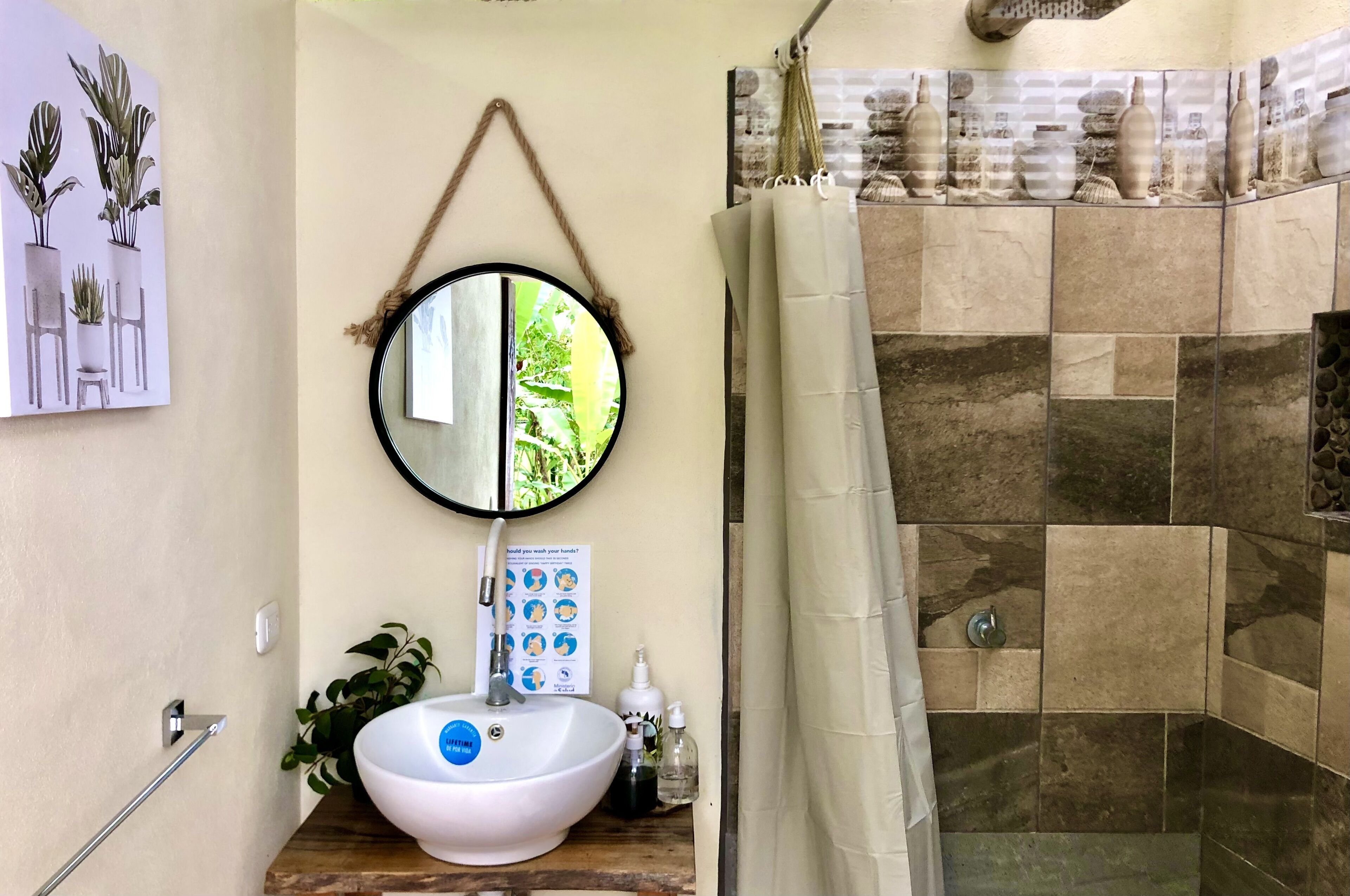 Un baño con un lavamanos blanco, un espejo, una cortina de ducha y una zona de ducha con azulejos.