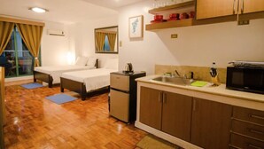 Ett kompakt hotellrum med ett litet pentry, två separata sängar, ett litet kylskåp och en mikrovågsugn.