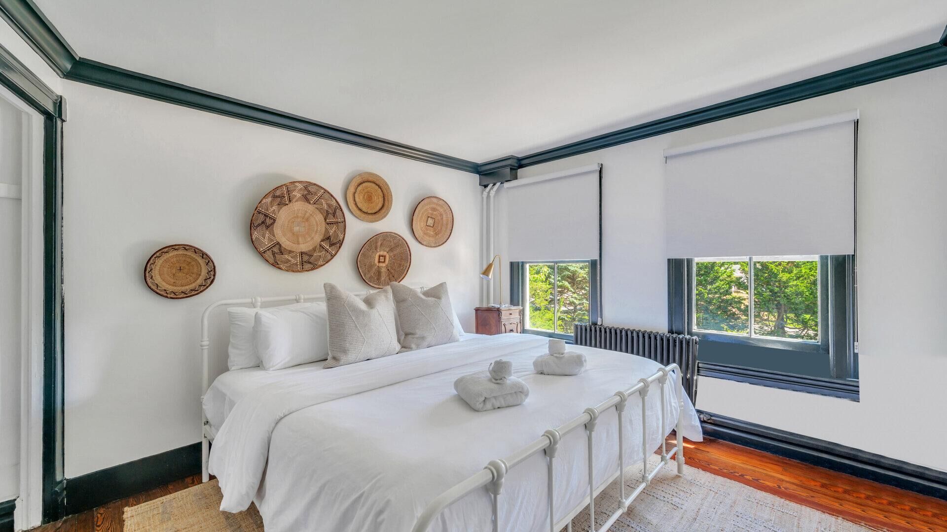 A bedroom with a large bed, white bedding, and several woven wall hangings.