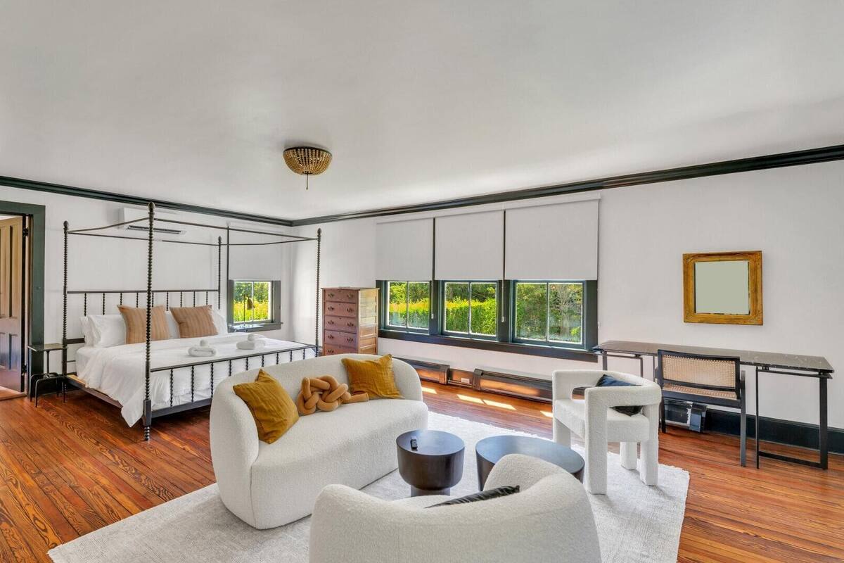 Quarto moderno com cama de dossel, um sofá, uma escrivaninha e vista para o verde lá fora.