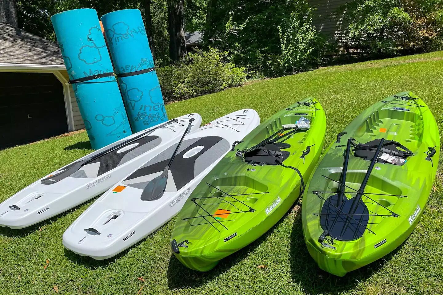 Three kayaks and two blue mats on a grassy lawn.