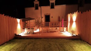 A well-lit outdoor patio area with a wooden fence, seating arrangements, and a small tree. - At the water's'edge "Nymphea (Saint-Barthelemy)