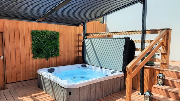A hot tub on a wooden deck with a pergola overhead, wooden stairs, and a green wall decoration. - At the water's'edge "Nymphea (Saint-Barthelemy)