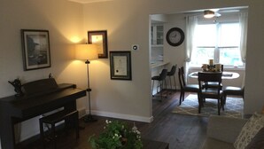 A living room with a piano, a lamp, a couch, and a dining area with chairs and a table.