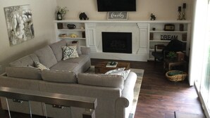 A living room with a sofa, a fireplace, a television, and shelves with decorative items.