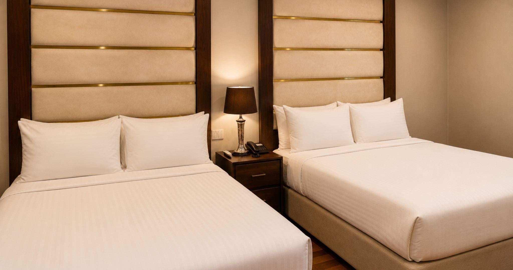 Quarto de hotel com duas camas, uma mesa de cabeceira com abajur e telefone.