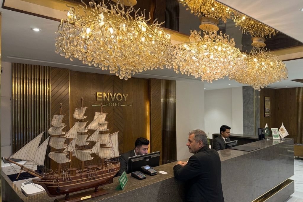 A hotel reception desk with a large ship model, a chandelier, and a sign that reads 'ENVOY HOTEL'.