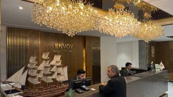 A hotel reception desk with a large ship model, a chandelier, and a sign that reads 'ENVOY HOTEL'.