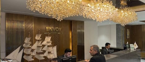 A hotel reception desk with a large ship model, a chandelier, and a sign that reads 'ENVOY HOTEL'.