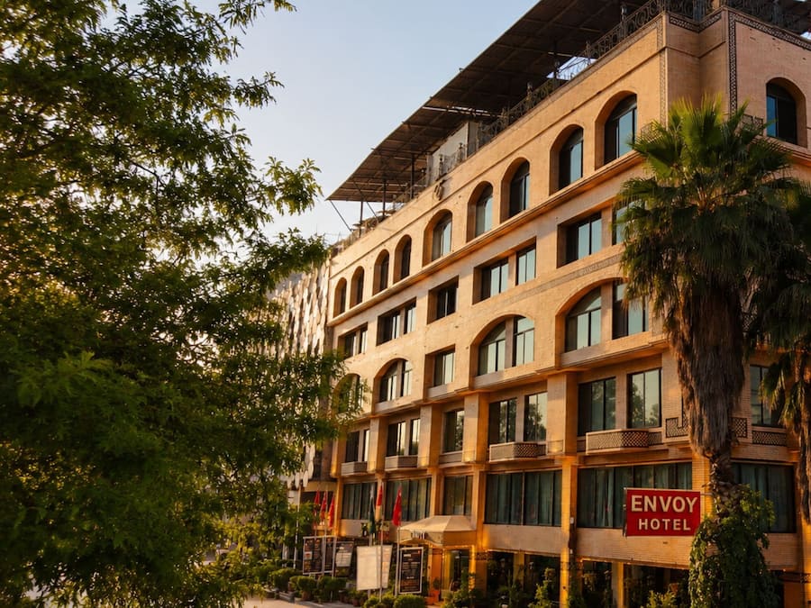 Un hotel de varios pisos con un letrero llamativo que dice 'ENVOY HOTEL' y un balcón con barandillas.