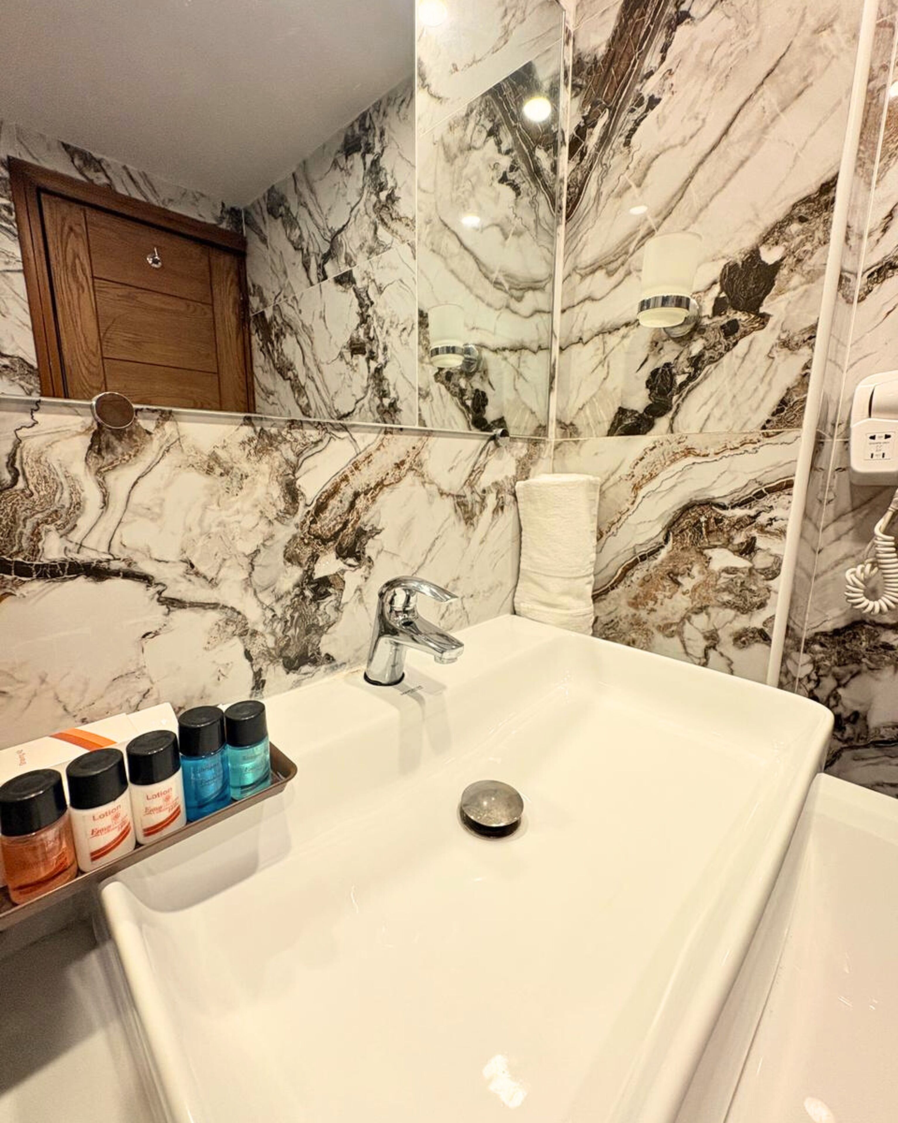 Un baño con pared de mármol, un lavabo blanco y un perchero para toallas.